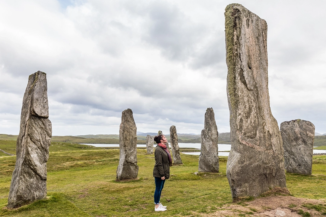 a woman looking up at tall rocks on a field